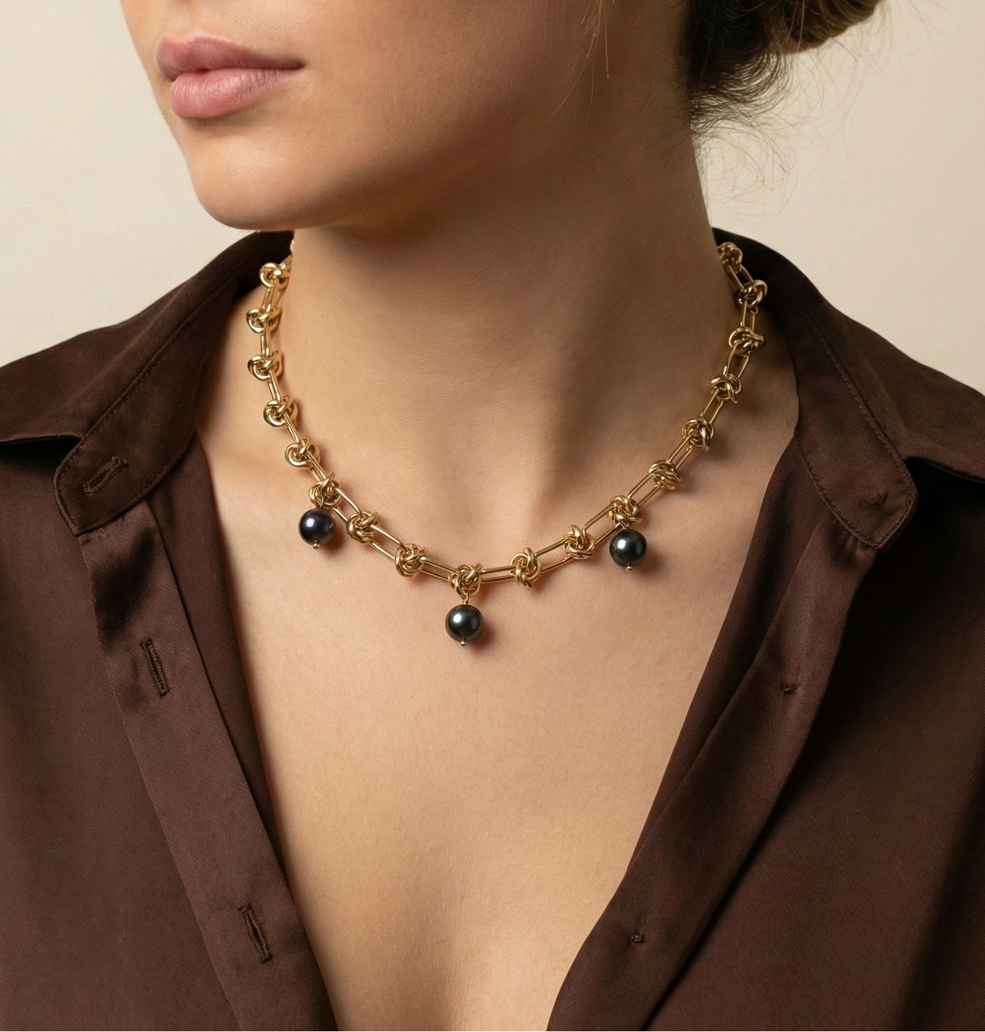 Woman wearing a Parisian-chic gold statement necklace with black pearls styled with a deep brown silk blouse