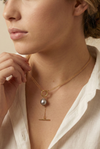 Model wearing a gold double-strand lariat necklace featuring a lustrous grey baroque pearl and toggle clasp, styled with a white linen shirt