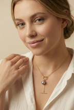 Model wearing a gold double-strand lariat necklace featuring a lustrous grey baroque pearl and toggle clasp, styled with a white linen shirt