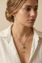 Model wearing a gold double-strand lariat necklace featuring a lustrous grey baroque pearl and toggle clasp, styled with a white linen shirt