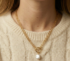 Close-up detail of a double-strand gold chain necklace featuring a lustrous white baroque pearl pendant and a T-bar toggle clasp, worn on the collarbone of a model