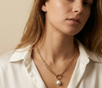 Close-up detail of a double-strand gold chain necklace featuring a lustrous white baroque pearl pendant and a T-bar toggle clasp