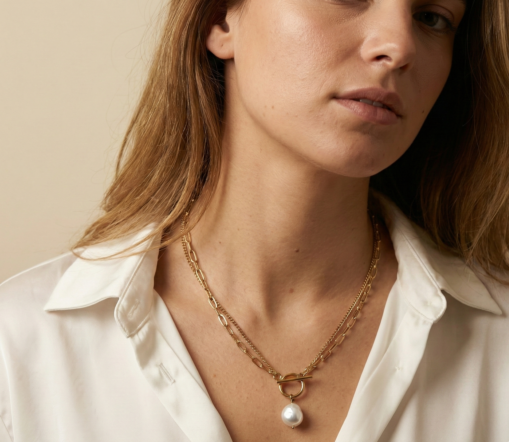 Close-up detail of a double-strand gold chain necklace featuring a lustrous white baroque pearl pendant and a T-bar toggle clasp