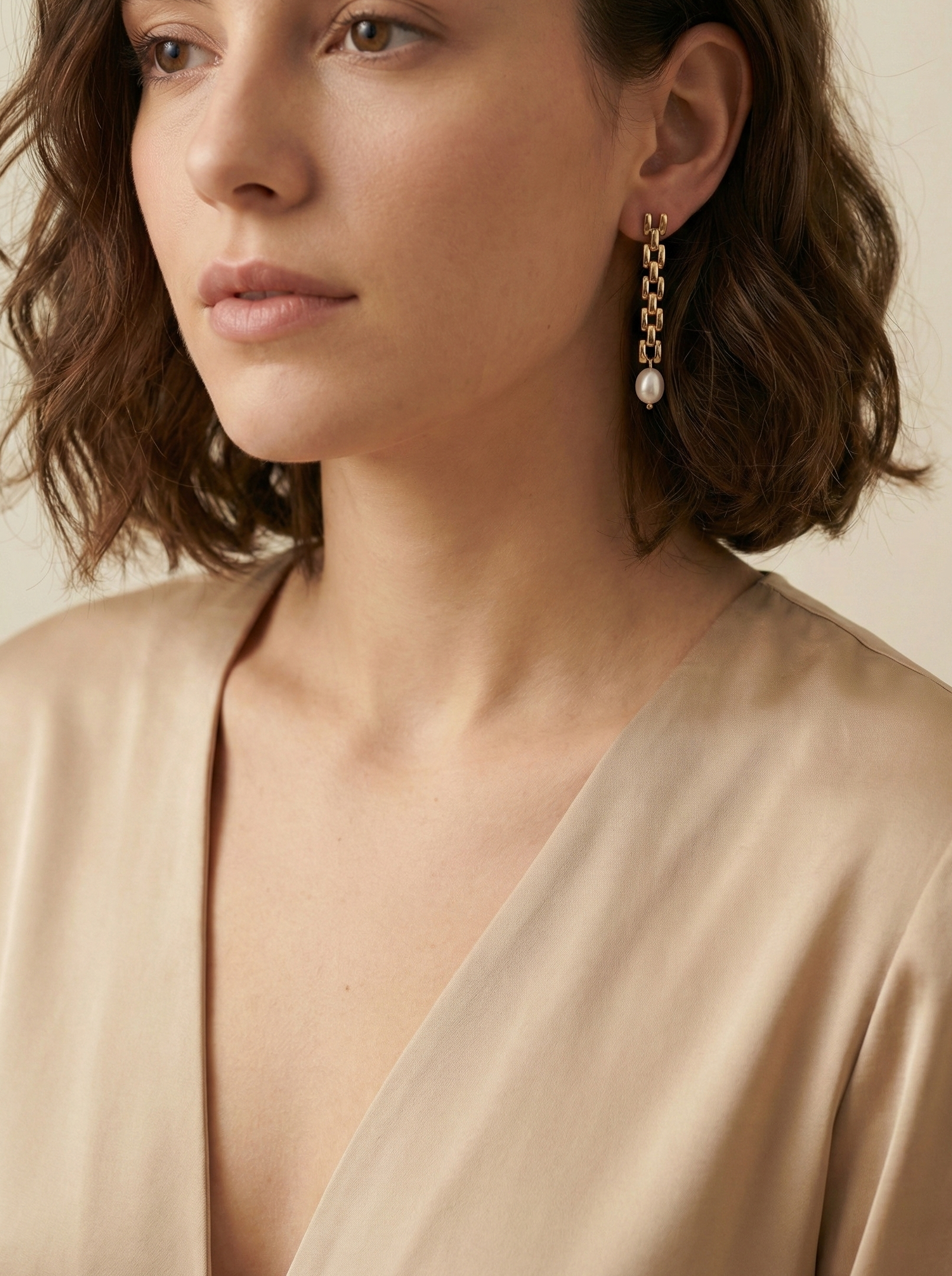 Gold rectangular link chain drop earrings featuring luminous white oval pearls on a beige silk background. Handcrafted Parisian pearl jewelry