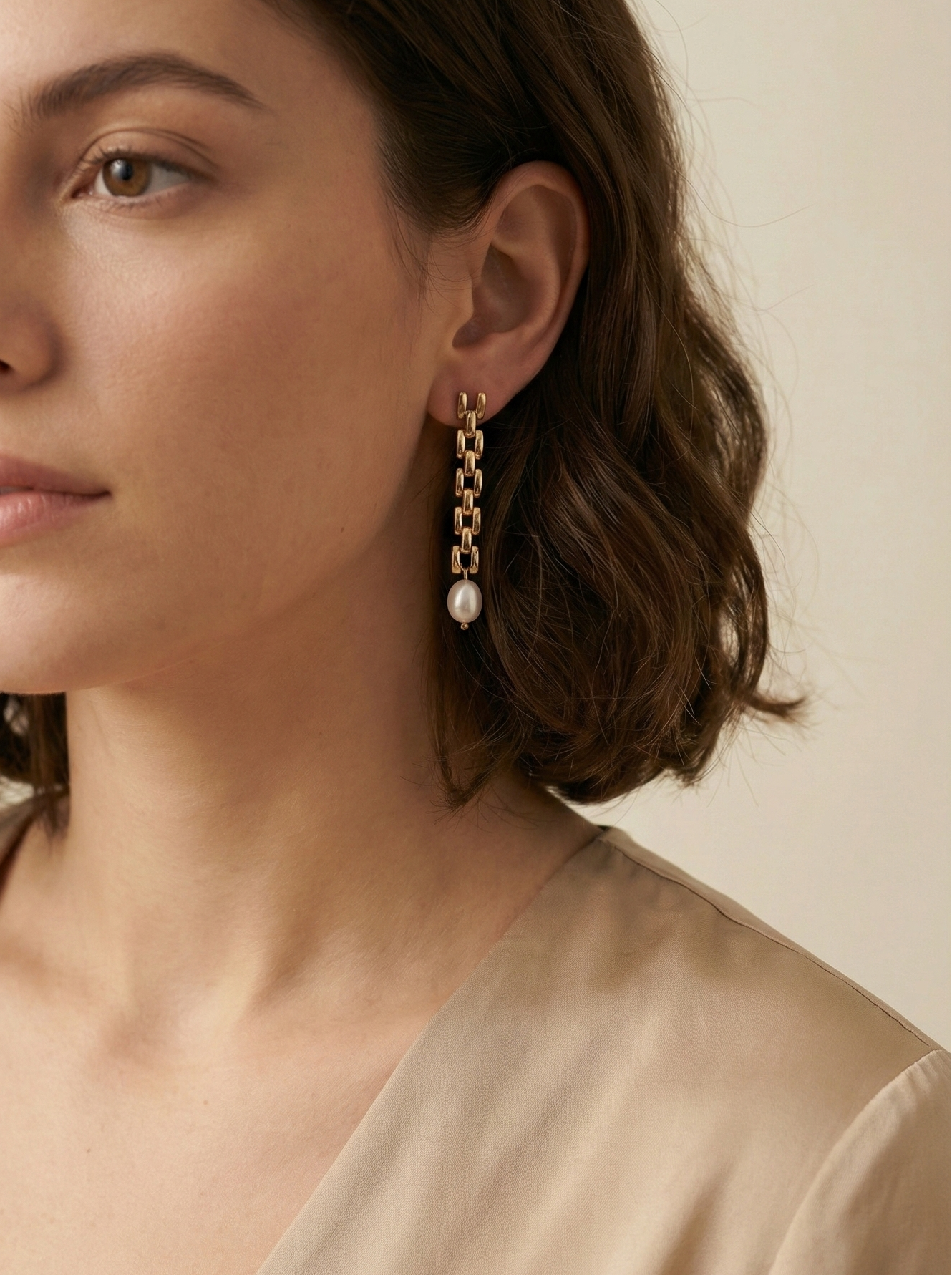 Gold rectangular link chain drop earrings featuring luminous white oval pearls on a beige silk background. Handcrafted Parisian pearl jewelry