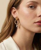 Close-up detail of textured gold interlocking hoop earrings featuring a lustrous metallic grey pearl drop. The design includes a beaded gold circle and polished gold links