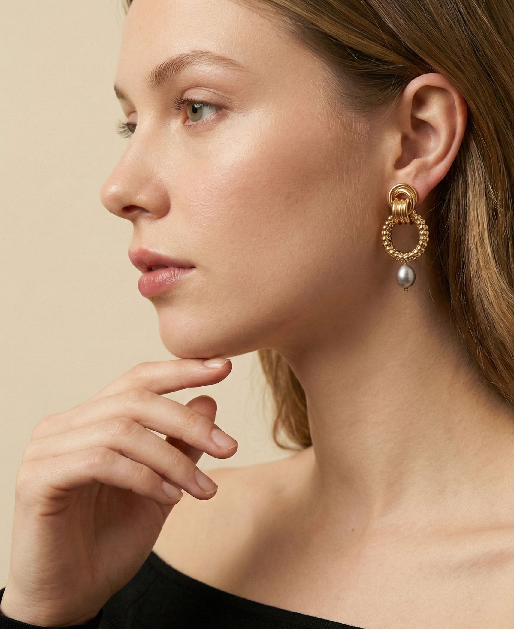 A model with blonde hair wearing elegant 18k gold plated link earrings with a grey pearl drop, styled with a minimalist black top for a luxury editorial look