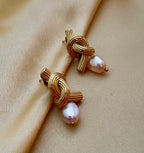 Close-up editorial photography of ribbed gold twisted knot earrings featuring a lustrous pink oval pearl drop