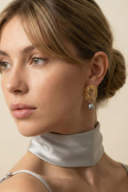 Close-up side profile of a blonde model with a low bun wearing gold concentric spiral statement earrings with a lustrous organic freshwater grey pearl drop
