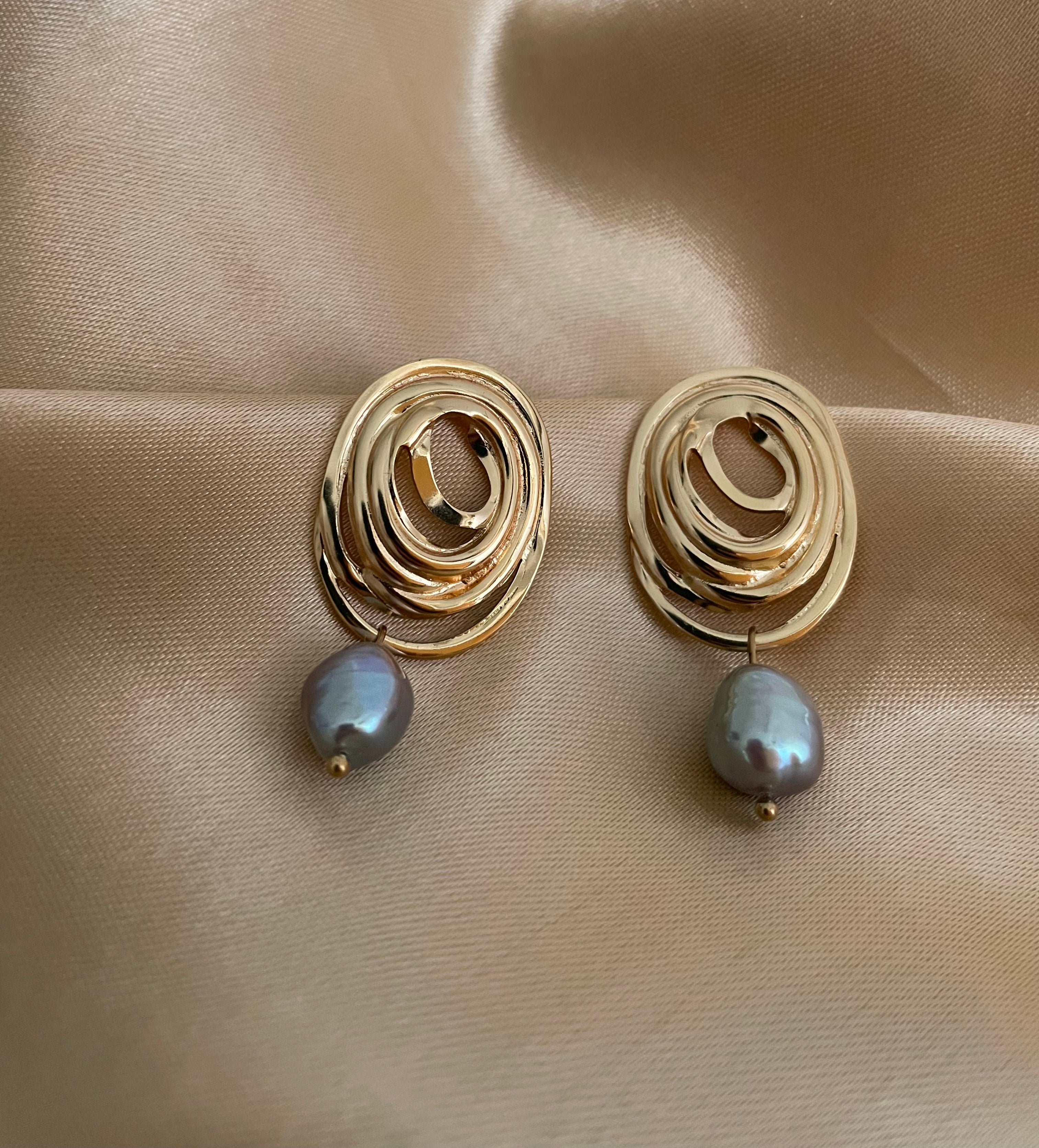 Close-up of a gold concentric spiral statement earrings with a lustrous organic freshwater grey pearl drop