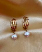 Luxury gold huggie earrings with white baroque pearl drop on model ear. High-luster freshwater pearl jewelry with triple-split gold hoop design in an editorial close-u