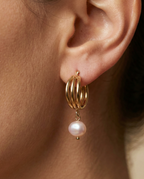 Luxury gold huggie earrings with white baroque pearl drop on model ear. High-luster freshwater pearl jewelry with triple-split gold hoop design in an editorial close-up