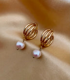 Close-up editorial shot of a gold triple-hoop huggie earring featuring a dangling white baroque pearl