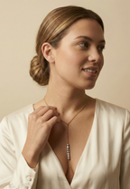 Close-up of a model wearing a delicate gold Y-necklace featuring a vertical drop of seven lustrous grey baroque pearls, styled with a deep V-neck ivory silk top