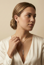 Close-up of a model wearing a delicate gold Y-necklace featuring a vertical drop of seven lustrous grey baroque pearls, styled with a deep V-neck ivory silk top