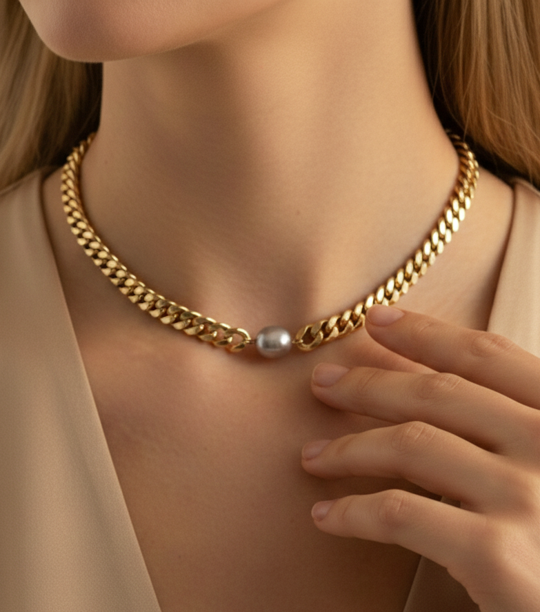 Close-up of a gold Cuban link chain necklace featuring a single, centered AAA grade grey baroque pearl on a model.