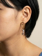 Close-up profile of a Korean model wearing luxury grey baroque pearl drop earrings with a sculptural gold double-oval link stud. The image highlights the iridescent nacre and organic shape of the pearl, styled with a blue knit top against a soft matte ivory background, representing high-end commercial jewelry photography