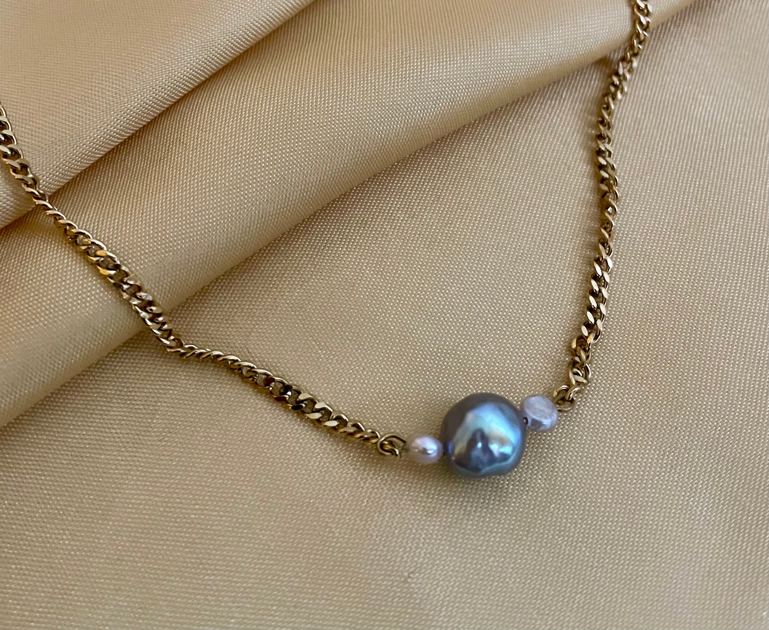 Close-up detail of an organic shaped grey pearl pendant on a gold curb chain, highlighting the iridescent nacre and handmade craftsmanship