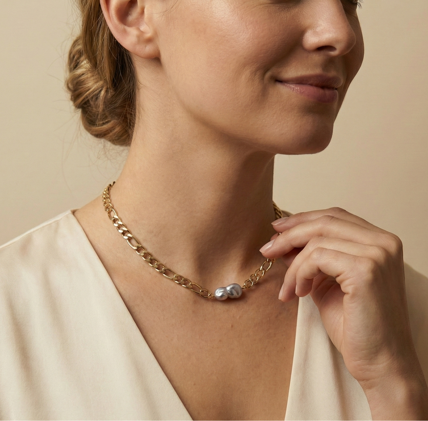 Detail shot of a grey Keshi pearl choker on a gold Figaro link chain. The pearl has a high silvery luster and flat organic shape, worn by a model in soft warm studio lighting.