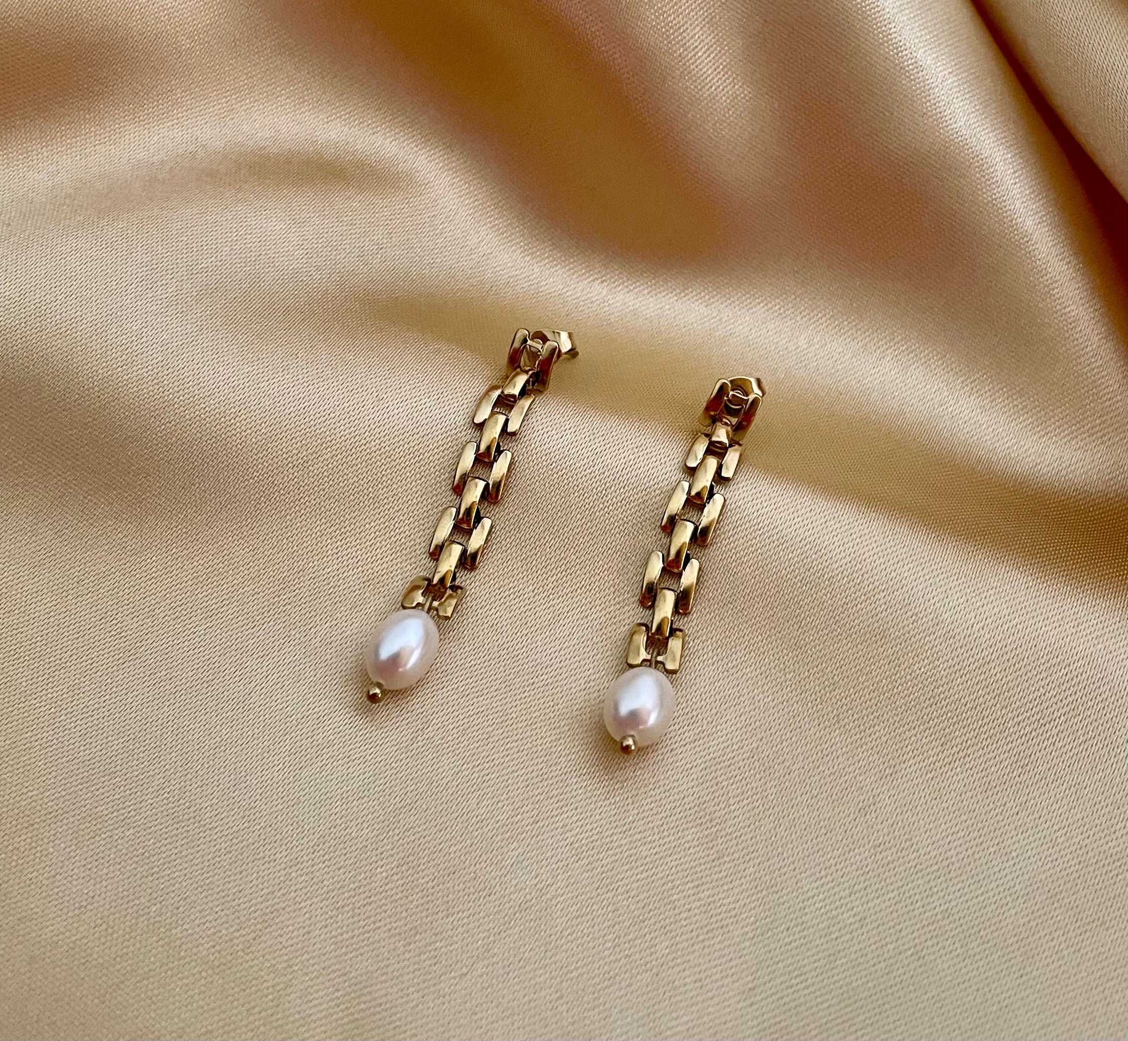 Close-up detail showing the high luster of a white oval pearl and the vintage-style gold link chain connection. Luxury jewelry design