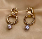 Close-up detail of textured gold interlocking hoop earrings featuring a lustrous metallic grey pearl drop. The design includes a beaded gold circle and polished gold links