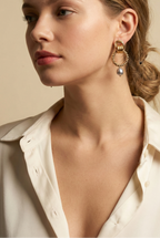 Close-up detail of textured gold interlocking hoop earrings featuring a lustrous metallic grey pearl drop. The design includes a beaded gold circle and polished gold links