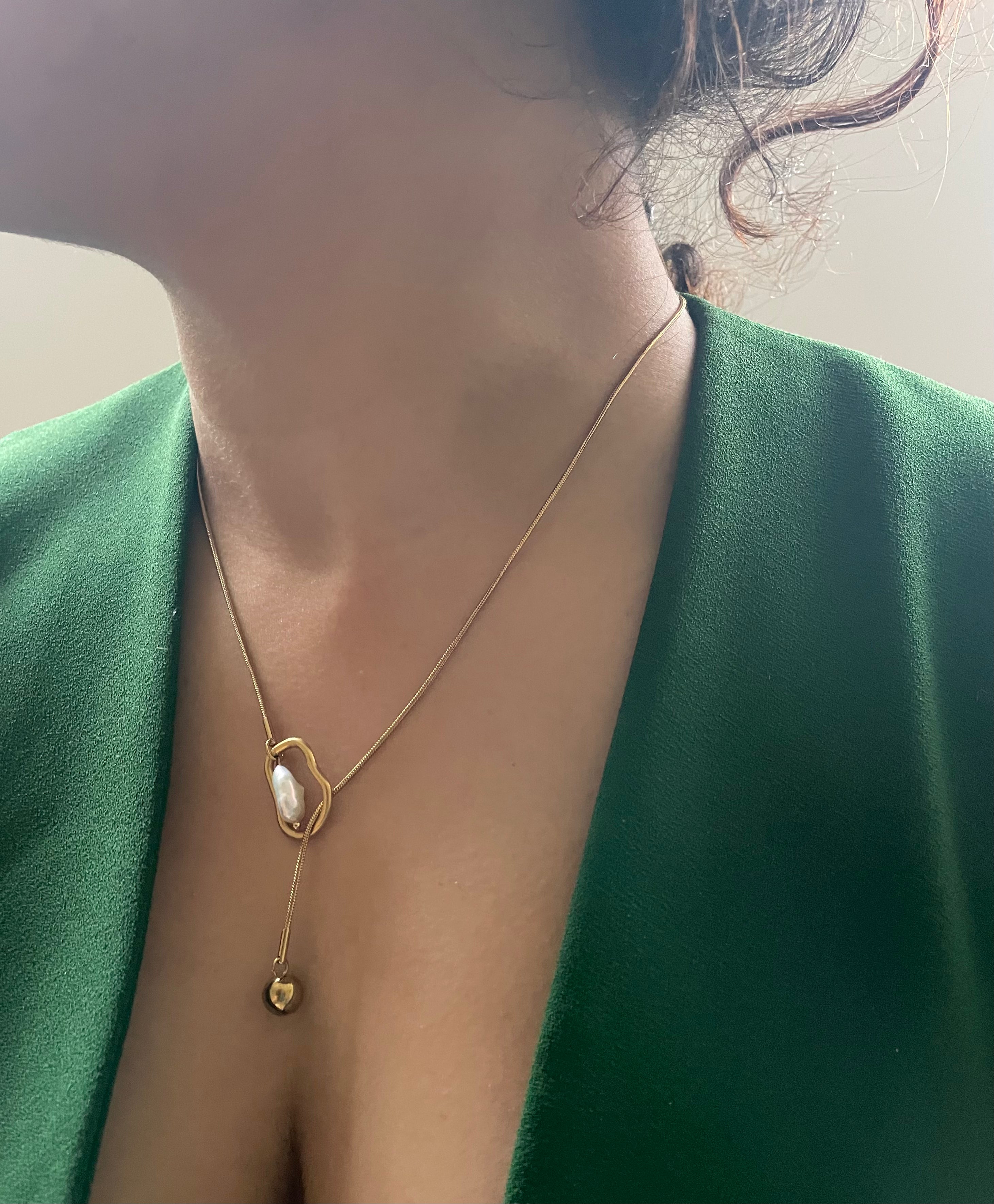 Gold necklace with a pendant worn by a person in a green outfit.