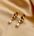 Close-up of gold chain link earrings featuring a lustrous oval white pearl drop. The earrings are shown on a model to demonstrate scale, featuring a high-polish gold finish and organic pearl shape