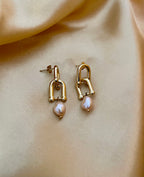 Fashion photography close-up of a gold and pink pearl earring worn on the ear, highlighting the jewelry's drop length and elegant shine