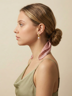 Woman wearing vintage-inspired gold knot statement earrings with dangling pink pearls. High-quality jewelry photography showing the detail of the ribbed gold texture and pearl luster against skin, styled with a casual-chic scarf.