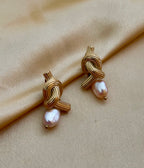 Close-up editorial photography of ribbed gold twisted knot earrings featuring a lustrous pink oval pearl drop