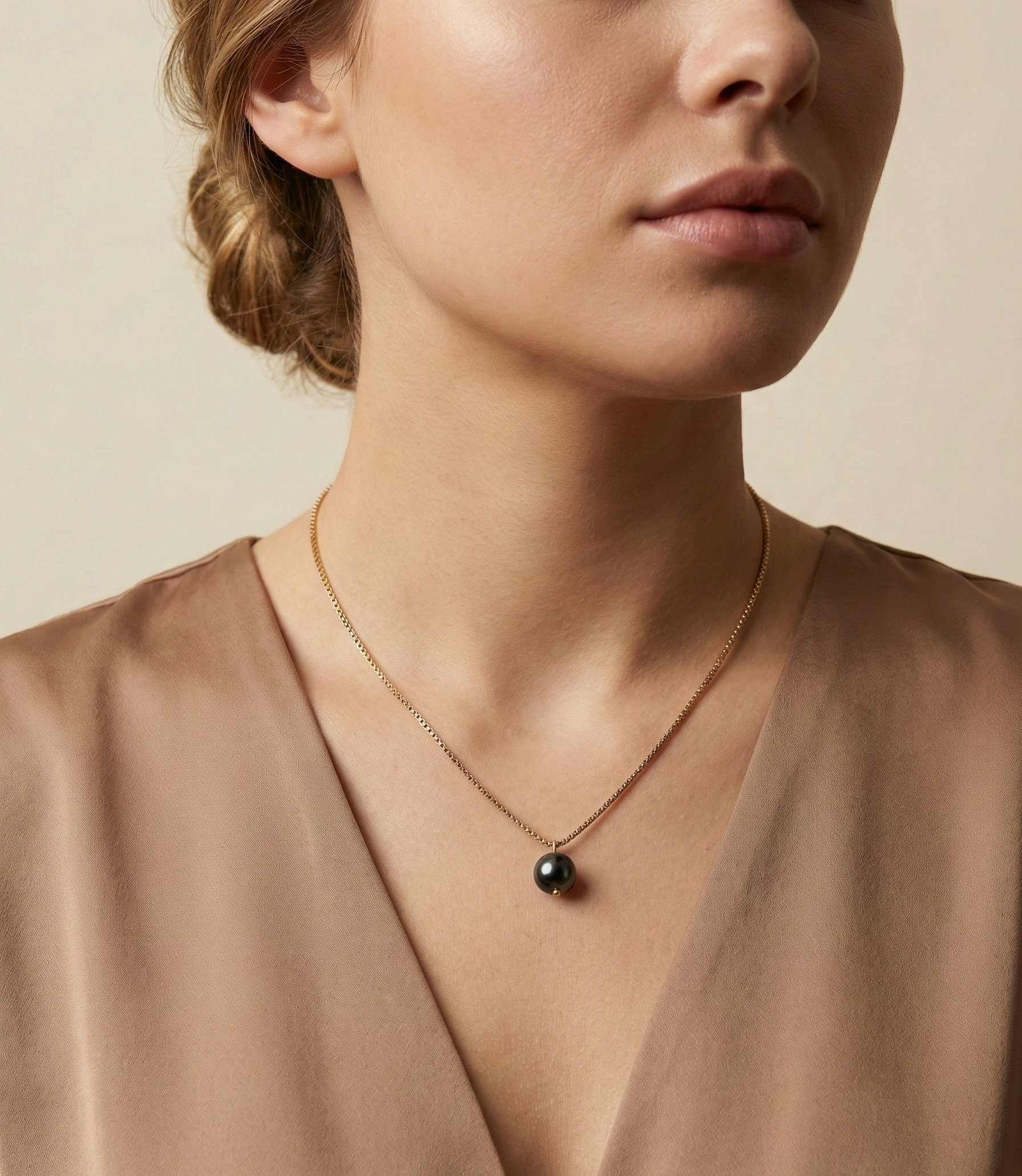 Elegant young woman wearing a minimalist black pearl necklace styled with a deep-neck brown silk blouse in soft studio lighting