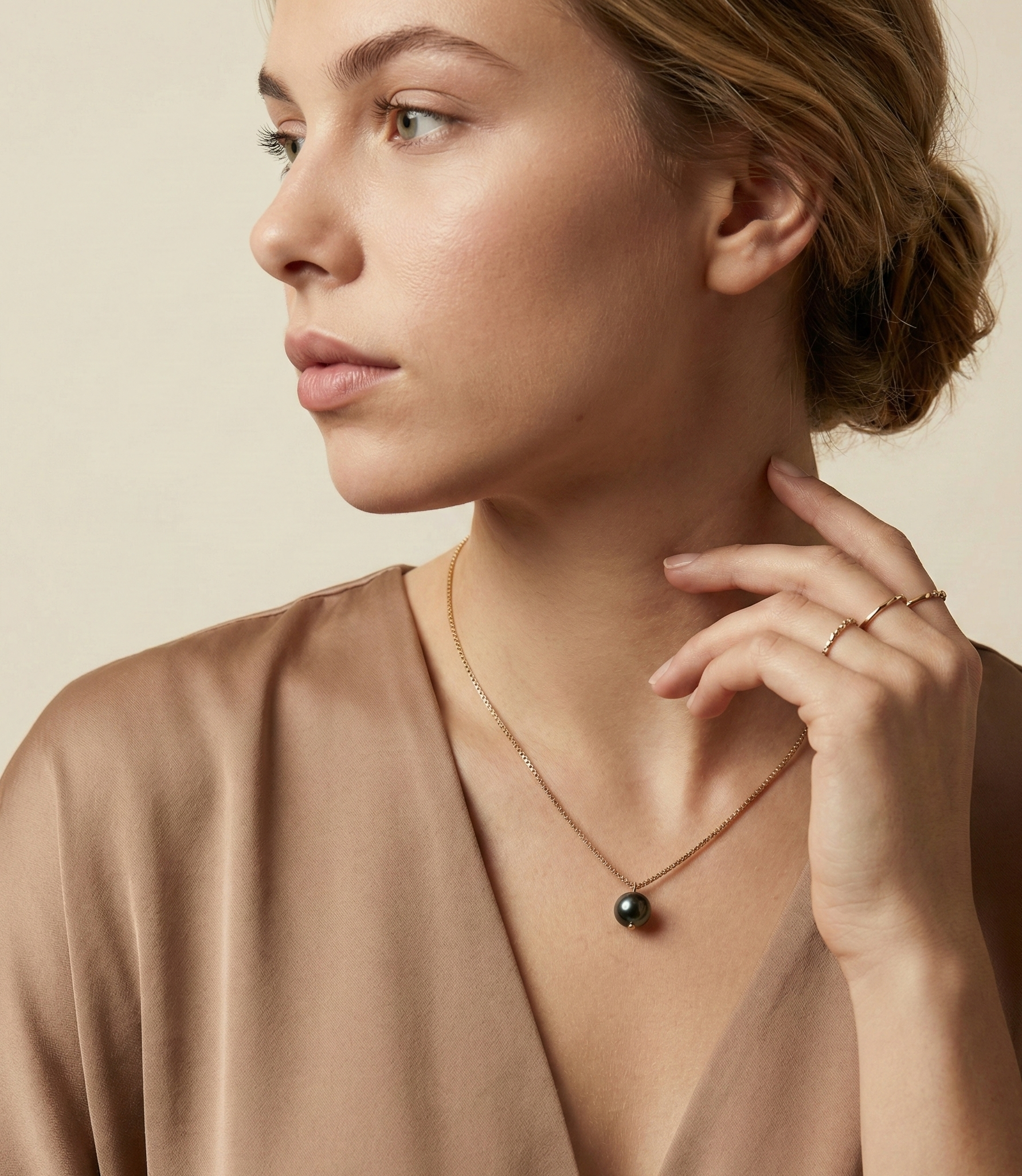 Dainty gold necklace featuring a single lustrous black pearl charm, displayed in a luxury jewelry portrait.