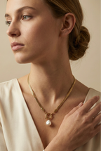 Model wearing an elegant gold chain necklace with a white baroque pearl drop and front clasp detail, styled with an ivory silk V-neck top