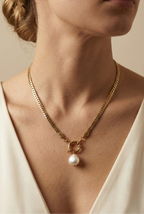 Model wearing an elegant gold chain necklace with a white baroque pearl drop and front clasp detail, styled with an ivory silk V-neck top
