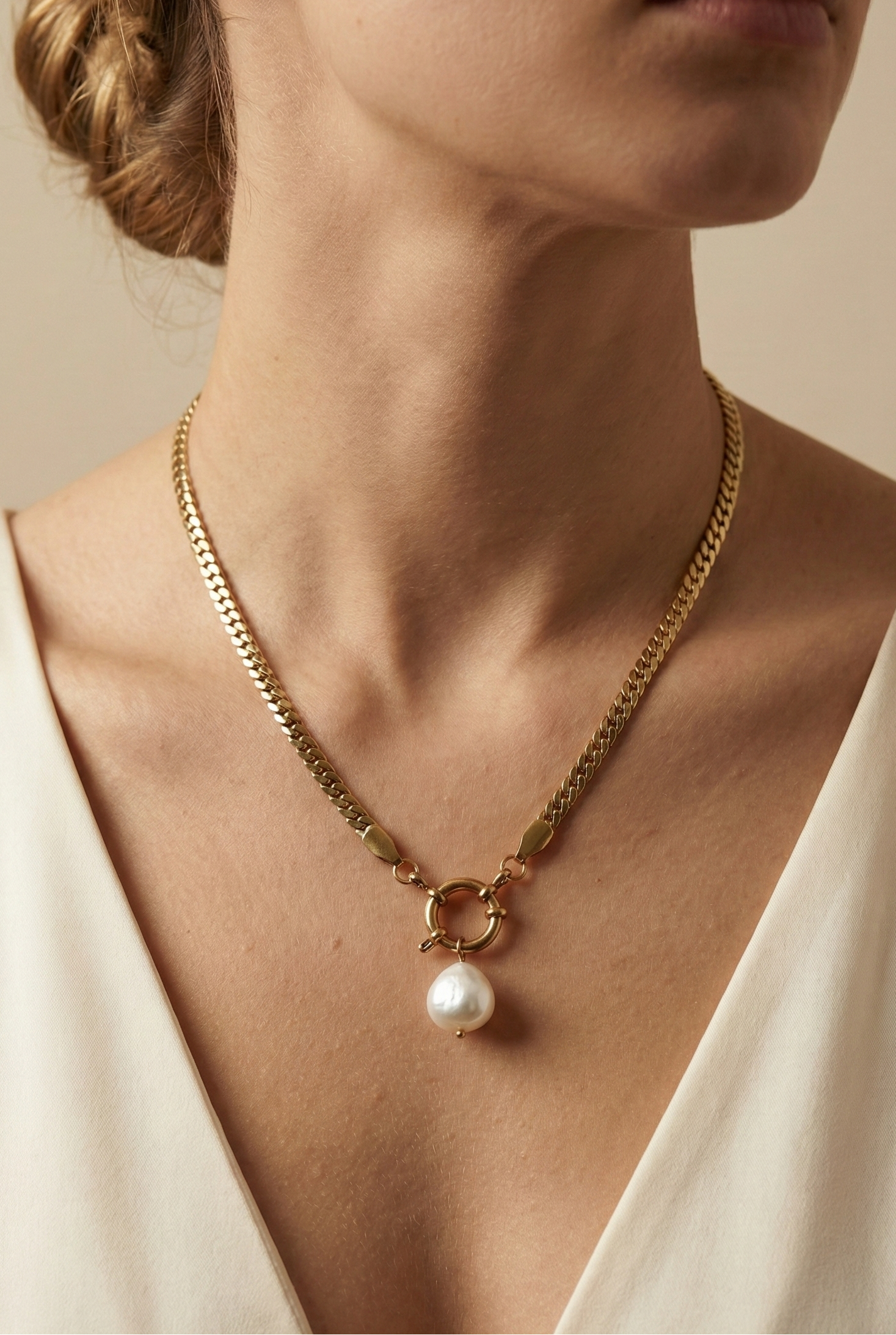 Model wearing an elegant gold chain necklace with a white baroque pearl drop and front clasp detail, styled with an ivory silk V-neck top