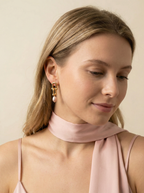Editorial portrait of a woman wearing gold link drop earrings with pink pearls, styled with a soft pink silk scarf