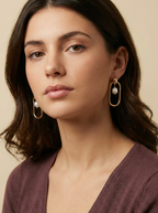 Editorial shot of a model wearing modern geometric gold hoop earrings with a floating freshwater pearl center, set against a warm ivory background