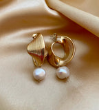Close-up of ribbed yellow gold shell earrings featuring a round white pearl drop