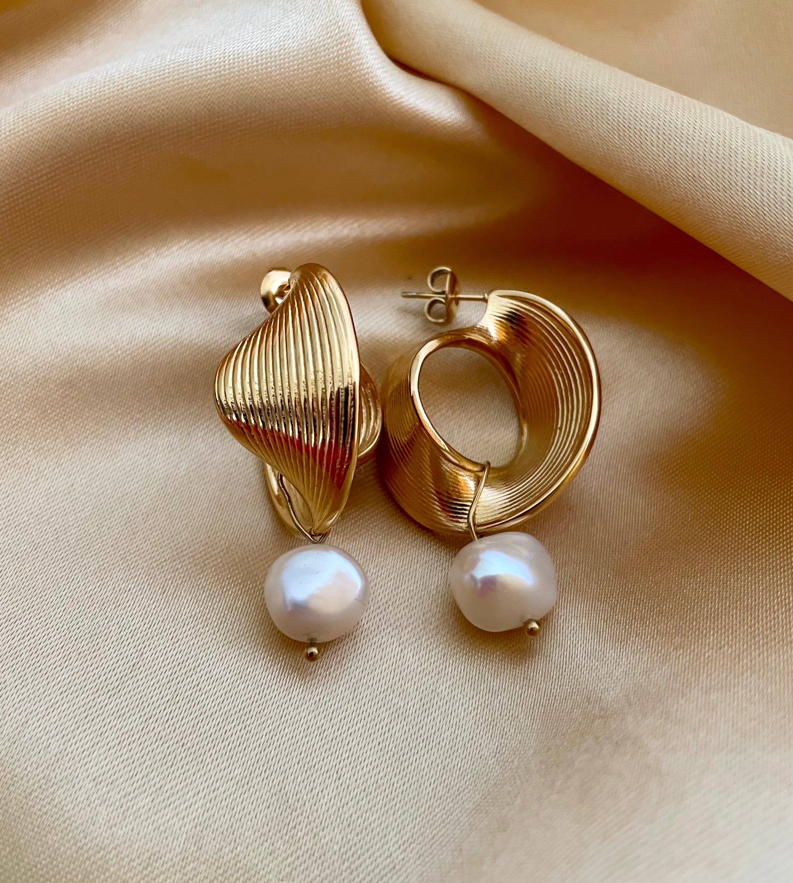 Close-up of ribbed yellow gold shell earrings featuring a round white pearl drop