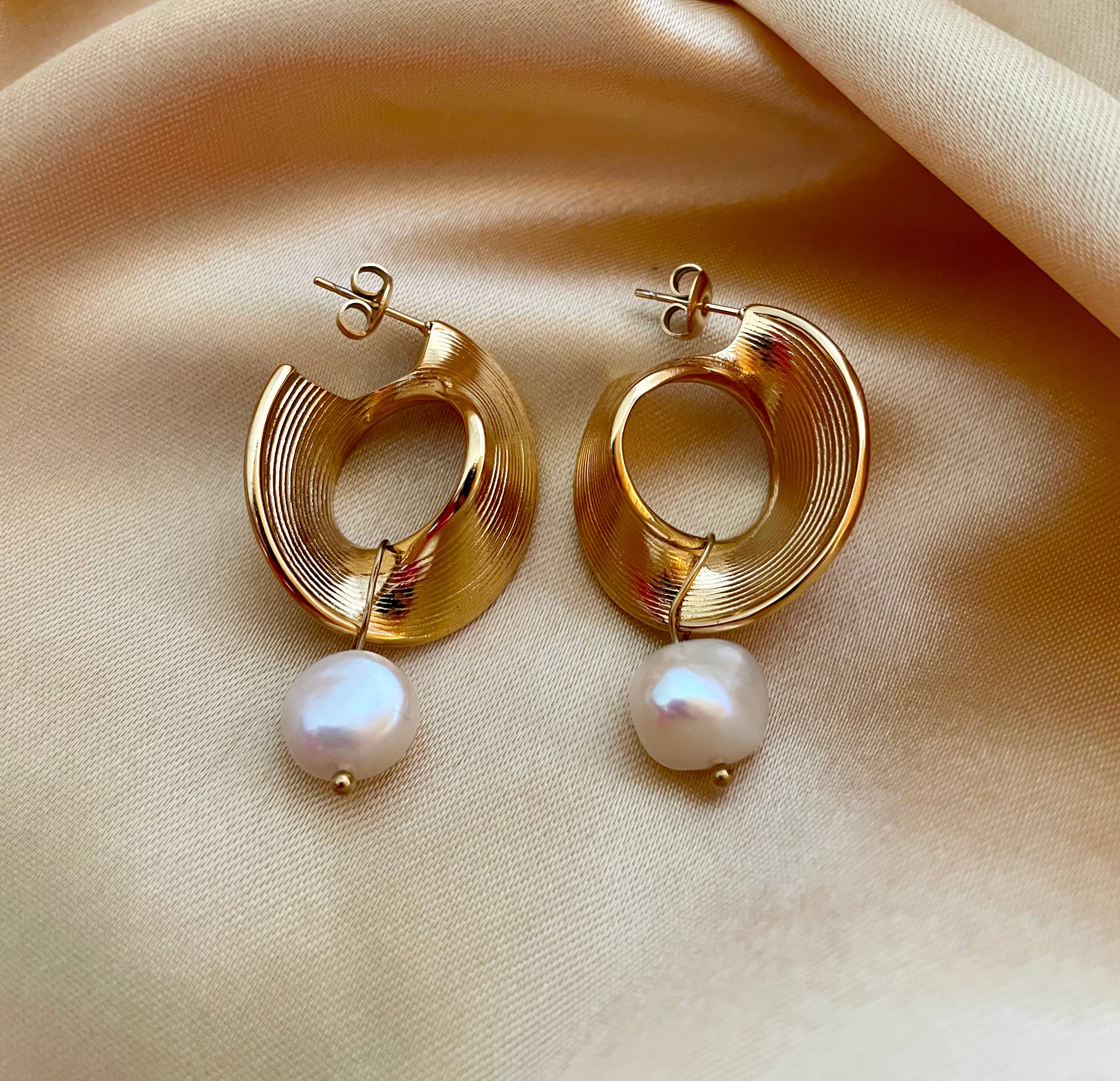 Editorial portrait of a woman wearing a white silk top styled with modern architectural gold earrings and lustrous pearl charms.