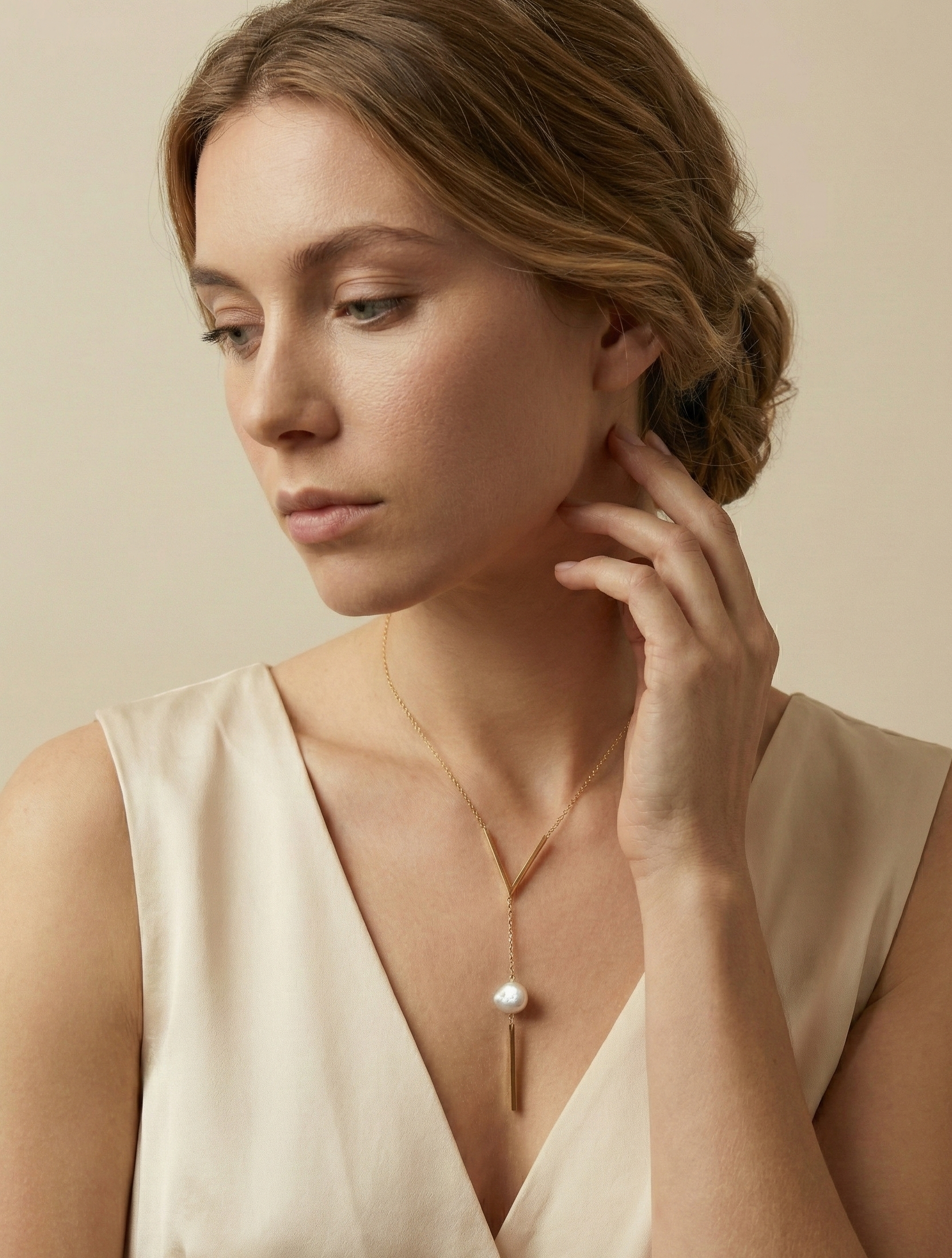 Model wearing a minimalist gold Y-necklace with a vertical bar pendant and organic white baroque pearl. Elegant geometric jewelry design