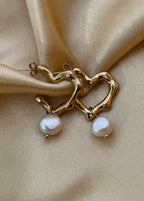 Close-up of an organic sculptural gold hoop earrings with a freshwater pearl drop. Modern 18k gold plated wavy hoops styled for everyday luxury