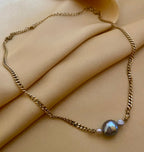 Close-up detail of an organic shaped grey pearl pendant on a gold curb chain, highlighting the iridescent nacre and handmade craftsmanship