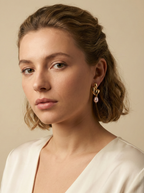 Editorial close-up of a model in a Parisian chic style wearing an ivory silk shirt. She is wearing unique, organic-shaped gold earrings featuring lustrous pink oval pearl drops