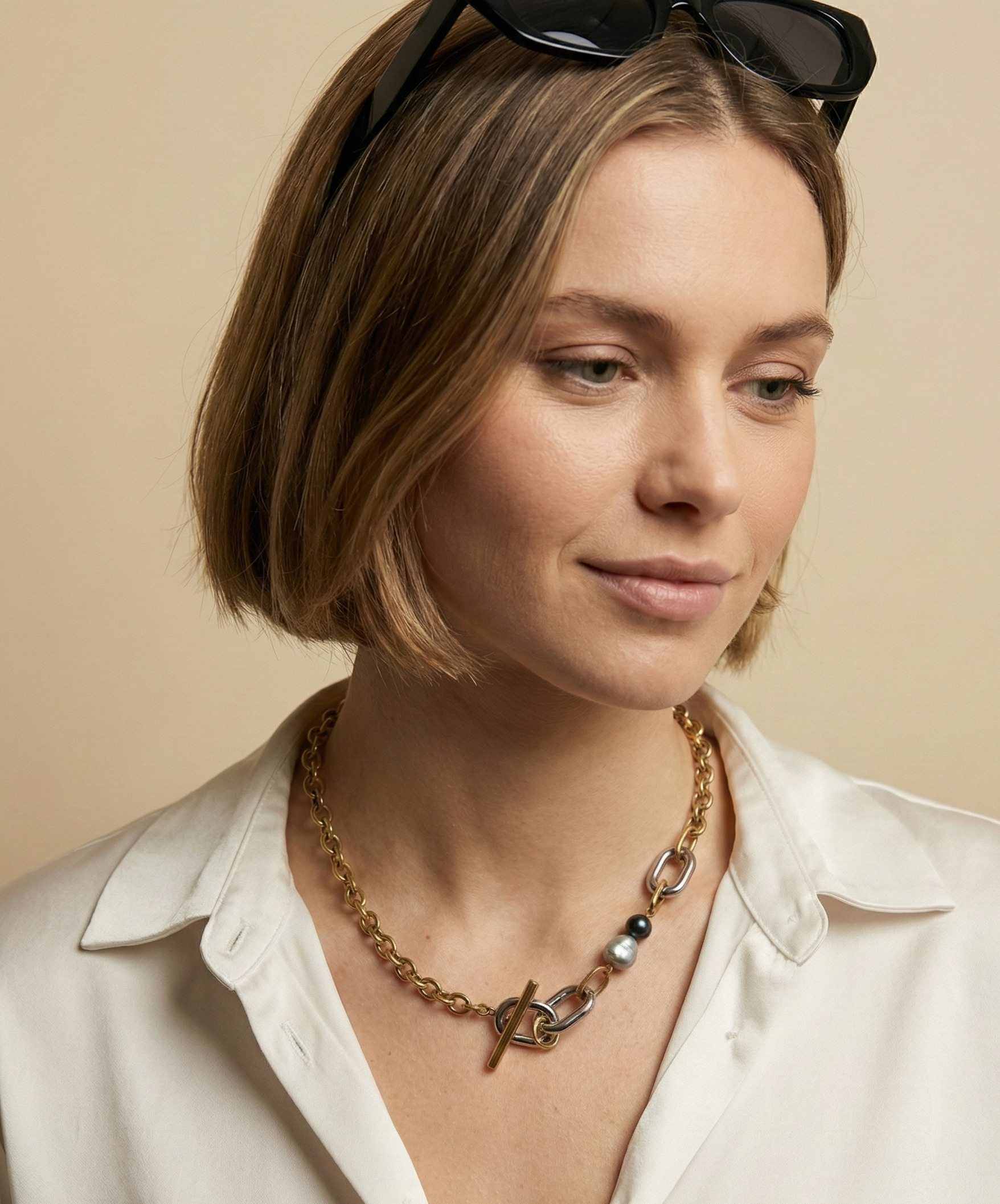 Woman wearing a statement baroque pearl necklace with gold and silver links and a T-bar toggle clasp, paired with a casual white silk shirt