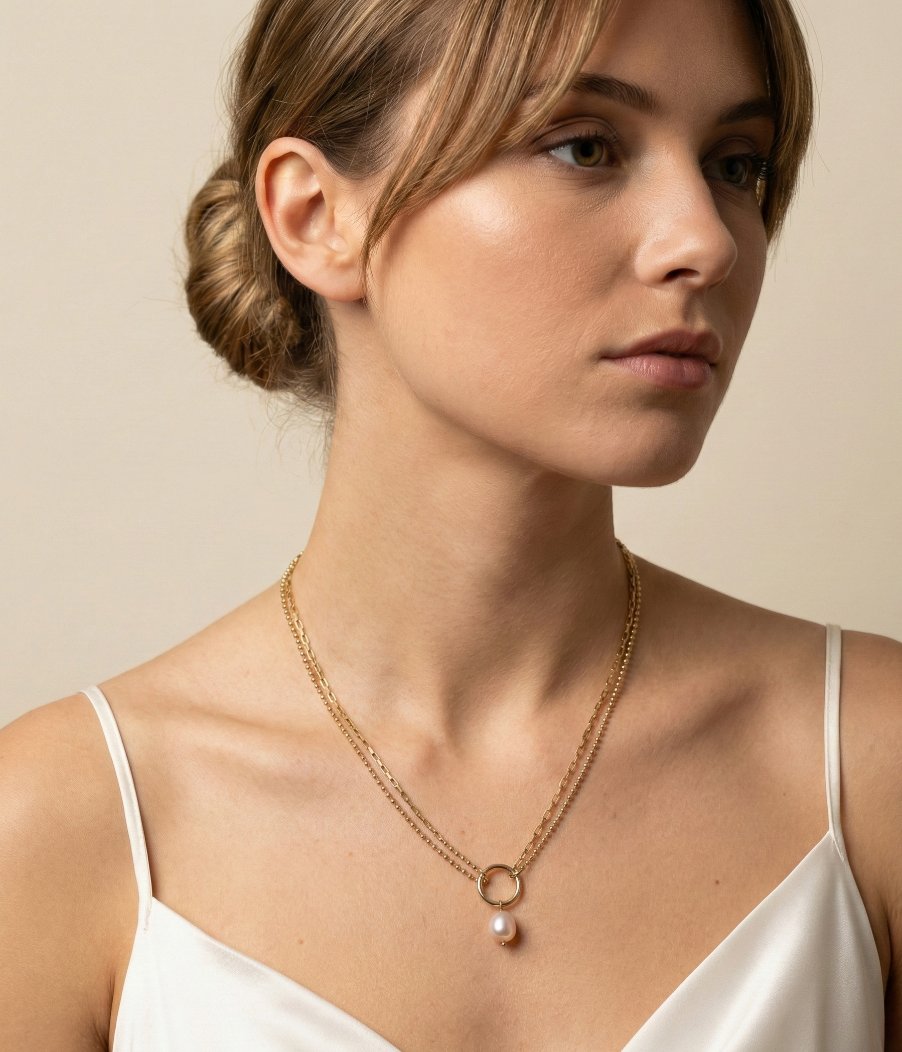 Woman wearing a gold necklace with a pearl pendant against a neutral background