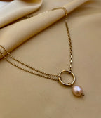 Gold necklace with a pearl pendant on a beige fabric background