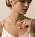 Woman wearing a gold necklace with a pearl pendant against a neutral background