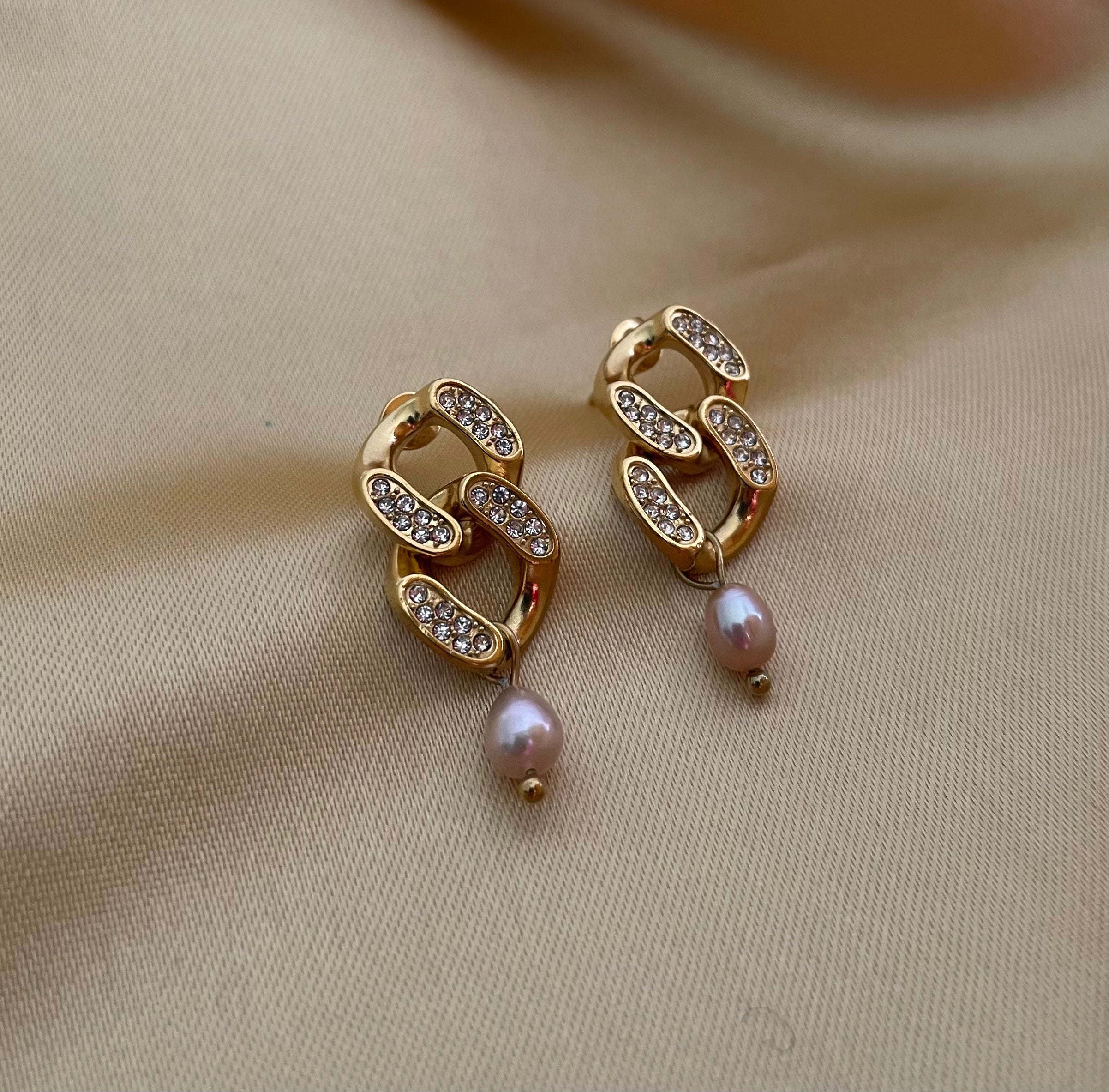 Gold chain earrings with pearl drops on a beige fabric background